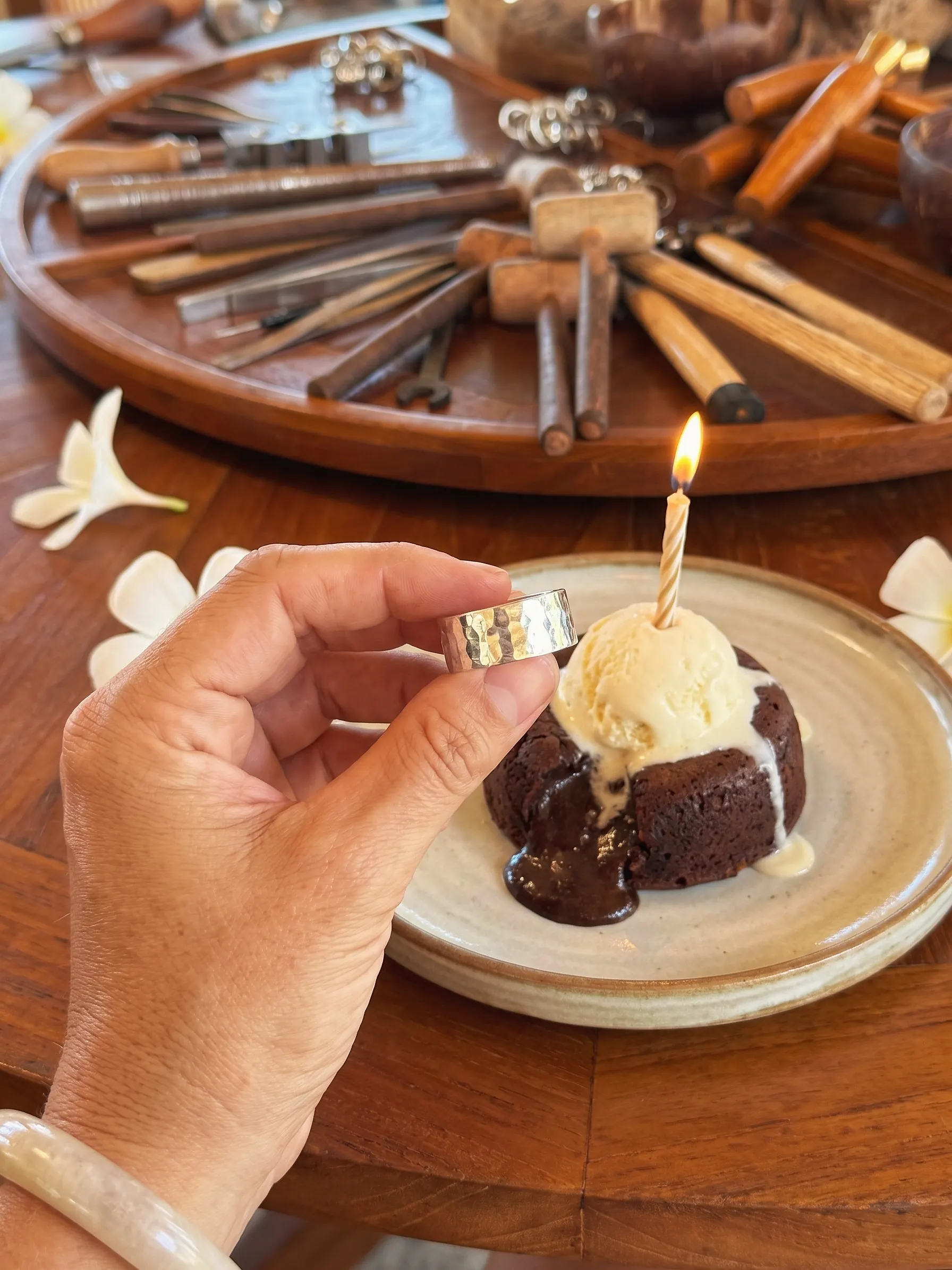 The birthday guest holds up a hammered silver ring beside a chocolate lava cake with a candle